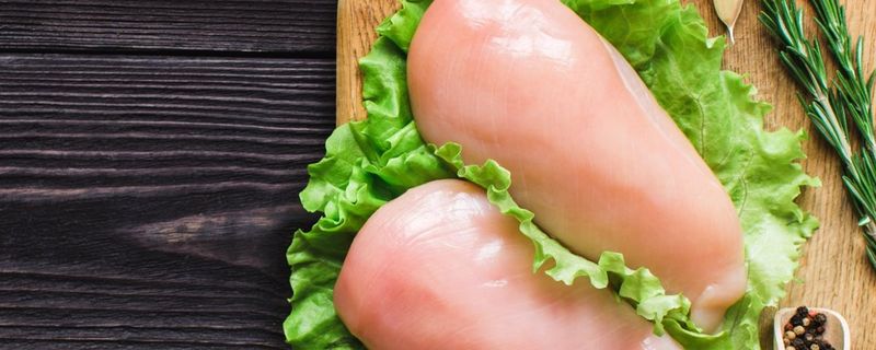 Boneless chicken breasts on a cutting board with fresh herbs